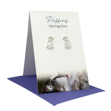 Load image into Gallery viewer, Silver penguin earrings on a branded card with a purple base