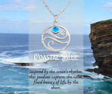 Load image into Gallery viewer, Silver pendant with blue gemstone on a necklace, set against a coastal background with ocean and cliffs.

