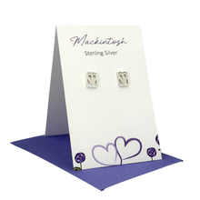 Load image into Gallery viewer, Silver heart-shaped earrings on a Mackintosh branded card with purple hearts design.
